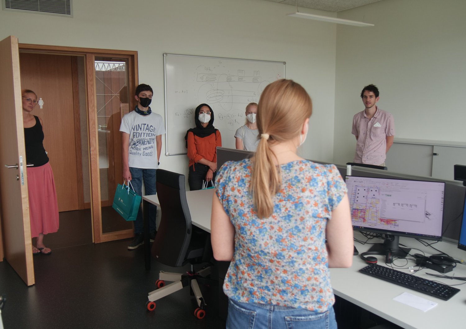 Four people standing in a room with a computer in it