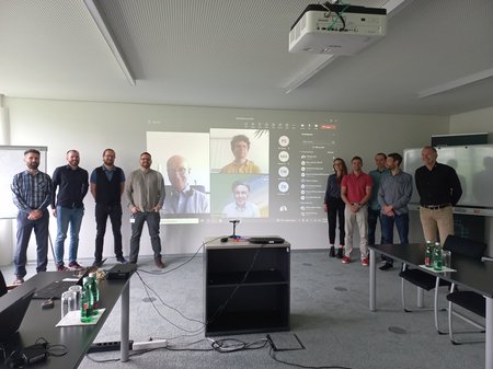 group picture at the kick-off, 9 people standing in front of a screen where you can see more people taking part online