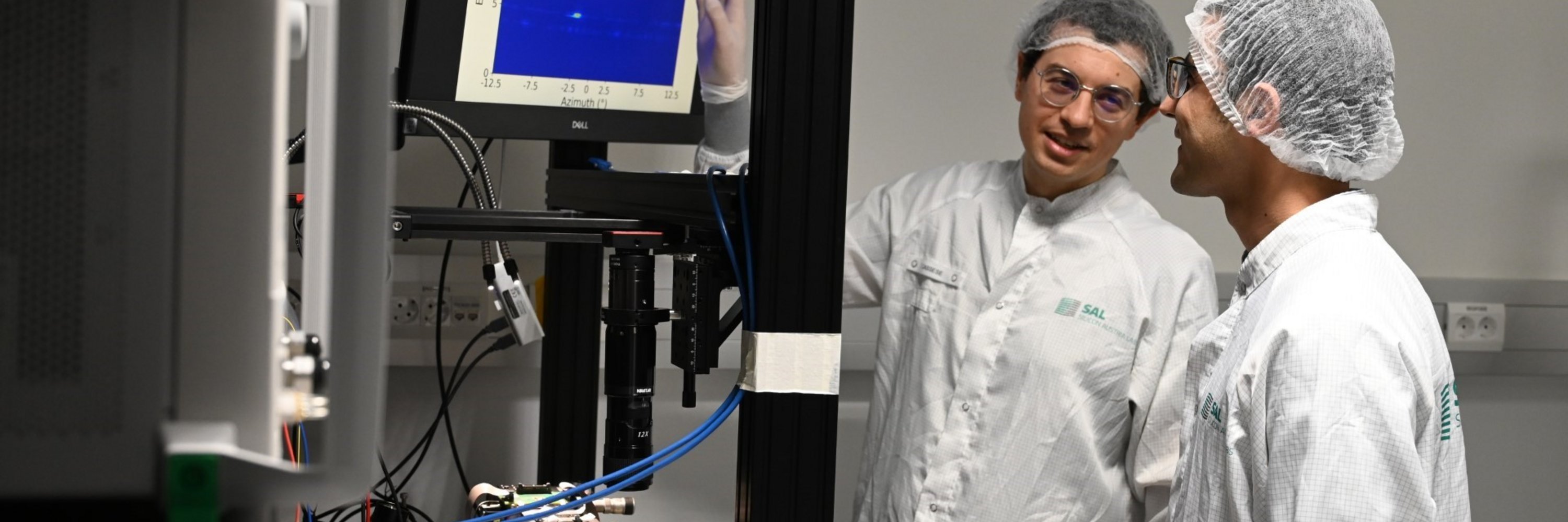 zwei Forscher in weißer Schutzkleidung stehen vor einem Computermonitor