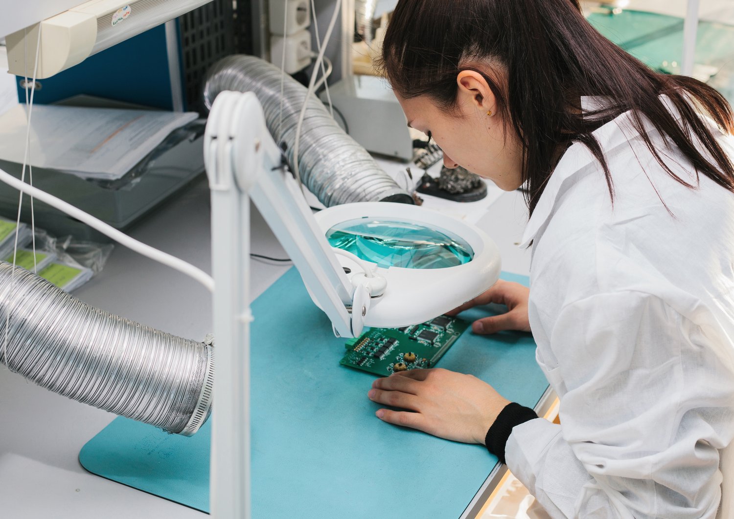 Eine Forscherin sitzt in einem Labor und schaut sich durch ein Vergrößerungsglas einen Chip an