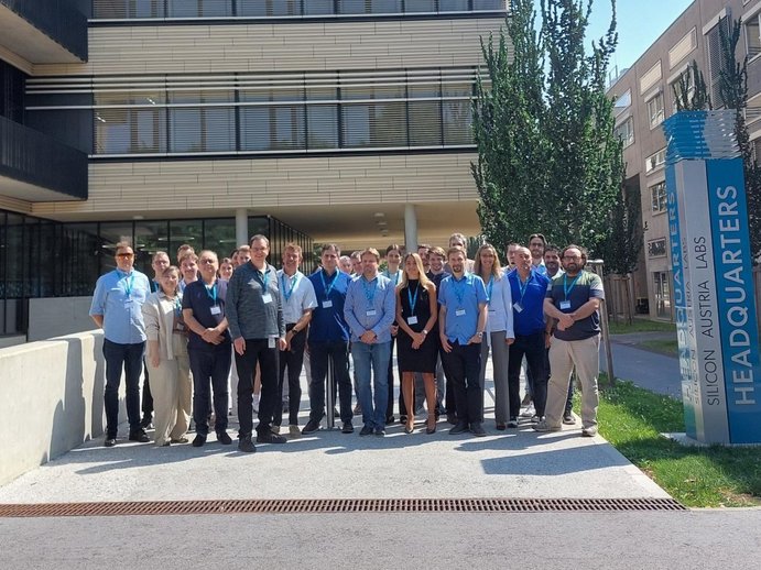 Group of approximately 30 people standing in front of the SAL building in Graz. To their right you can see a pillar that says "Silicon Austria Labs". 