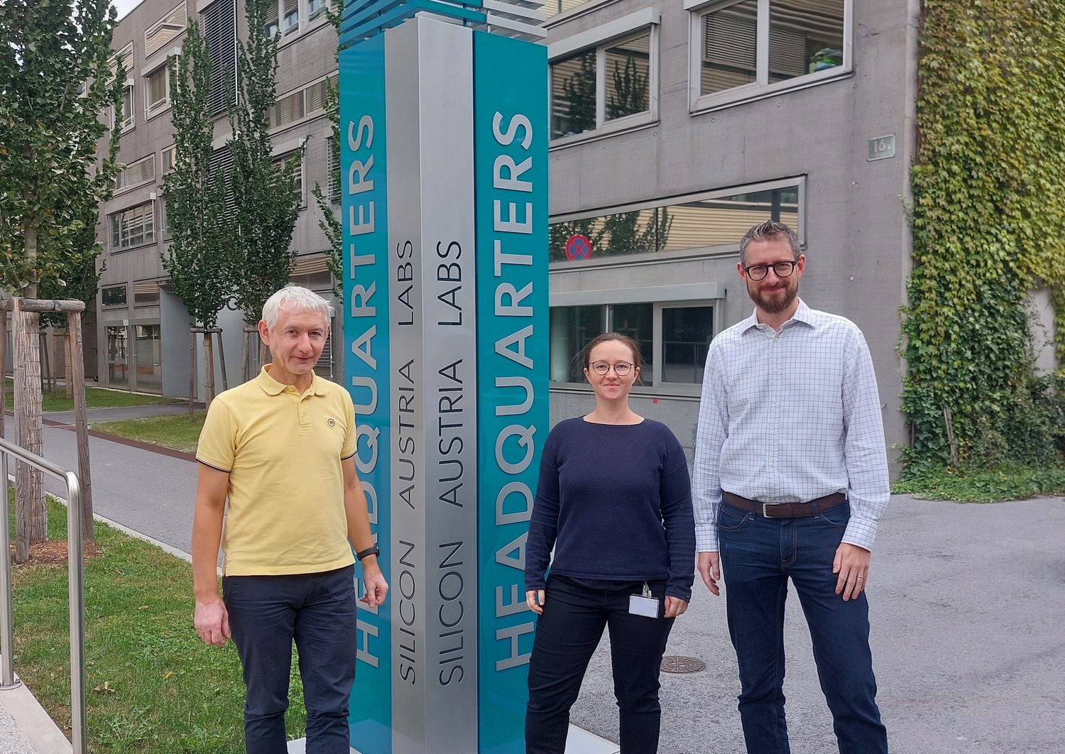 Rudolf Heer, Katrin Unger und Marco Deluca vor einer Säule vor dem SAL-Gebäude in Graz. Die Säule ist türkis und darauf steht "Silicon Austria Labs Headquarters". 