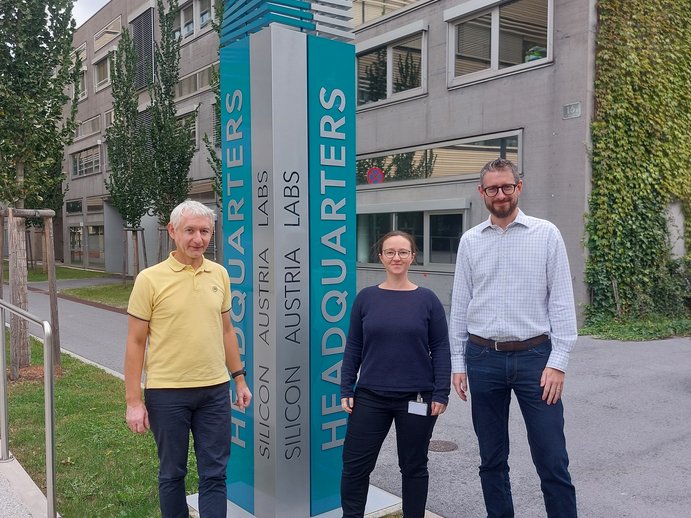 Rudolf Heer, Katrin Unger und Marco Deluca vor einer Säule vor dem SAL-Gebäude in Graz. Die Säule ist türkis und darauf steht "Silicon Austria Labs Headquarters". 