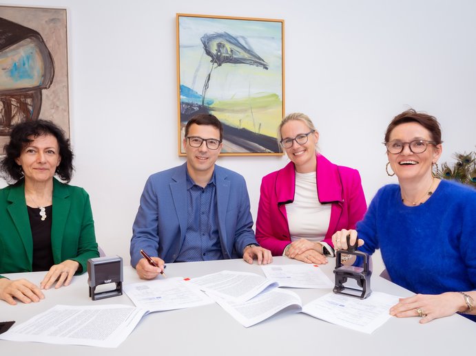 4 Personen sitzen an einem Tisch, vor ihnen ein unterzeichneter Vertrag