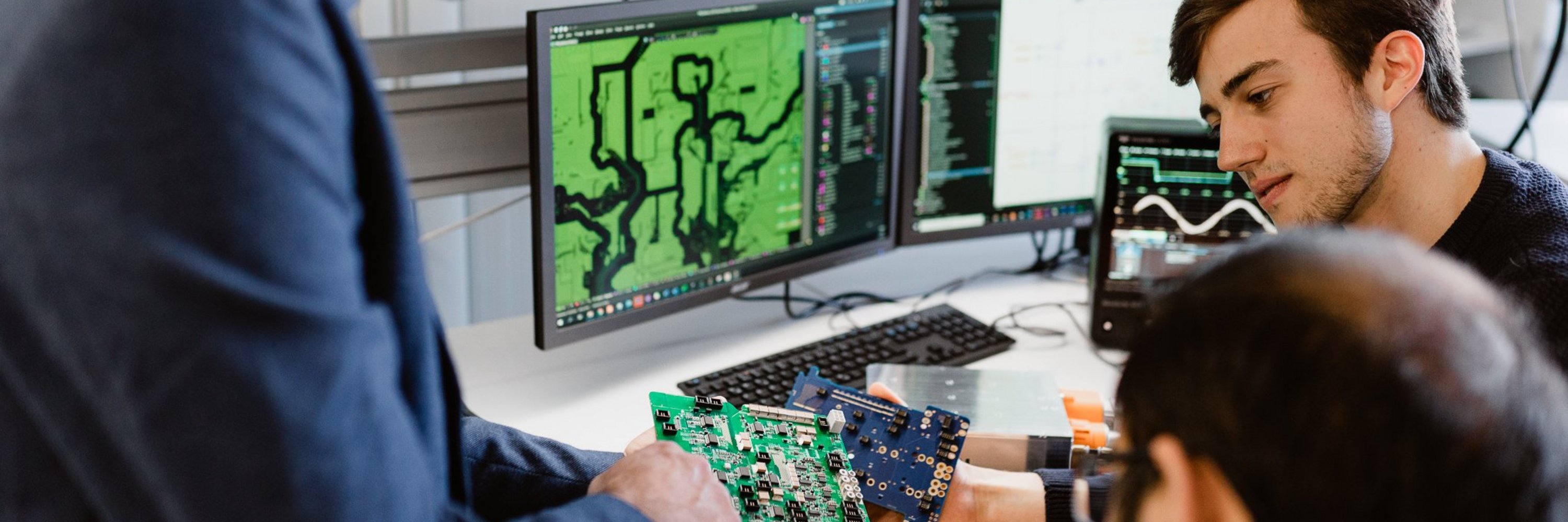 Three researchers with a printed circuit board in the lab